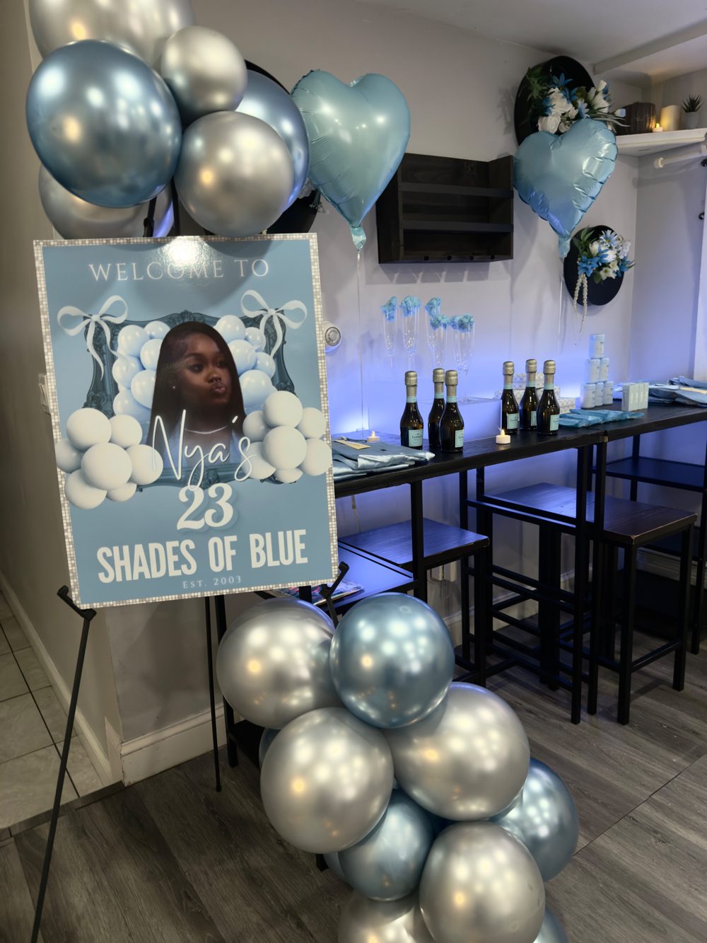 Custom Shades of Blue welcome sign on an easel beside a blue and silver balloon column and a champagne table
