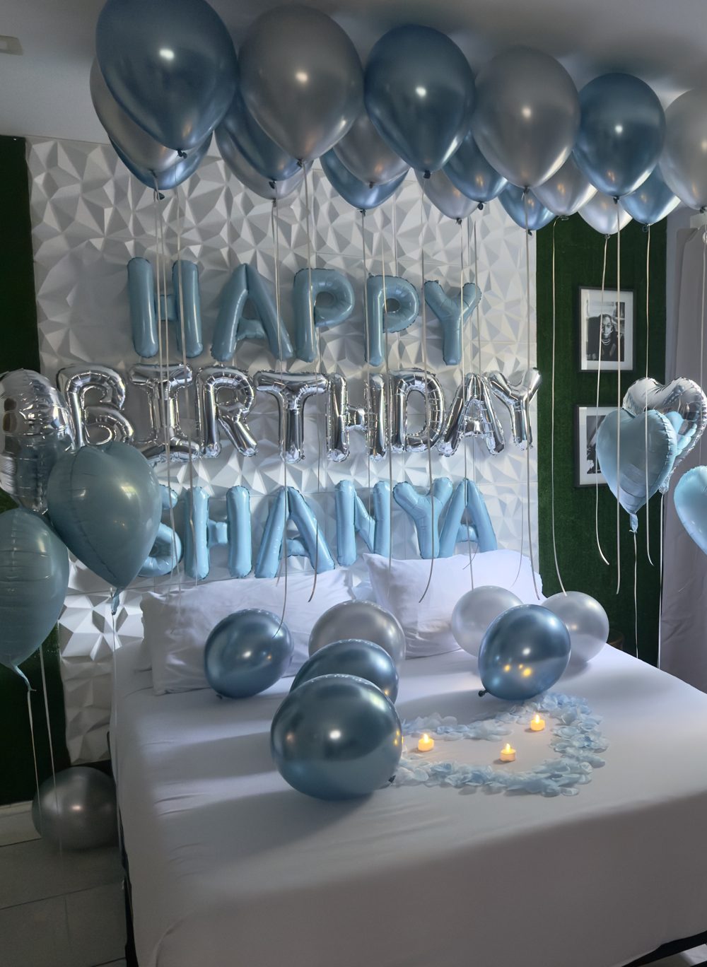 Suite styled with blue and silver balloons, a Happy Birthday name banner, and a rose petal heart with candles on the bed